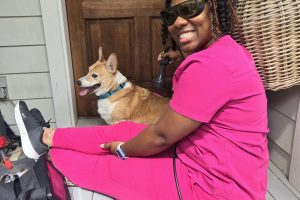 Corgi sitting outside next to vet technician who is administering laser therapy to dog
